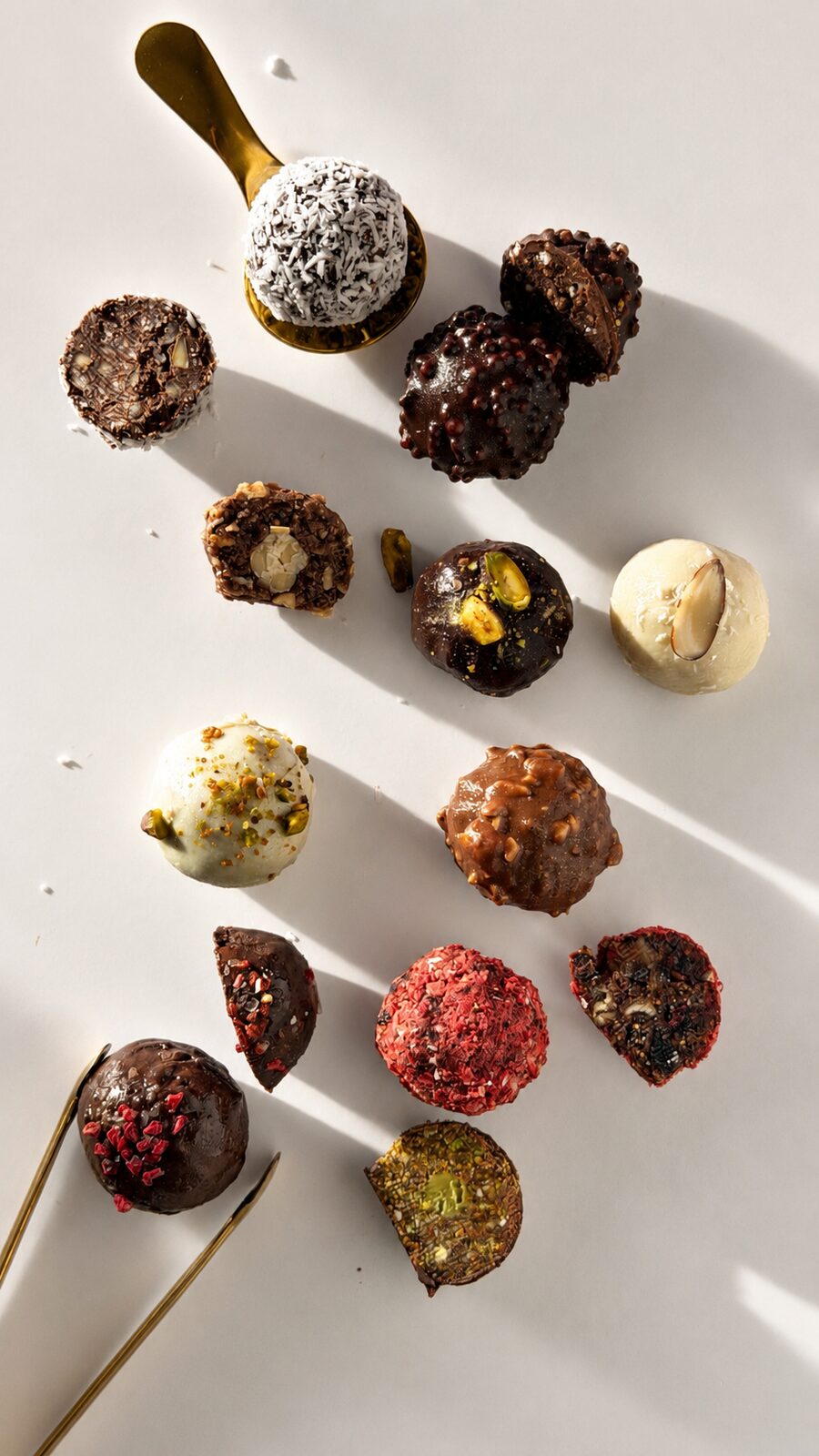 Handcrafted chocolate candies scattered on a white surface with a gold spoon of coconut flakes