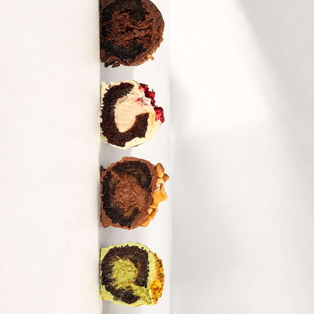 A selection of cream-filled royal dates coated in Belgian chocolate, cut to show pistachio, chocolate, berry and coconut fillings