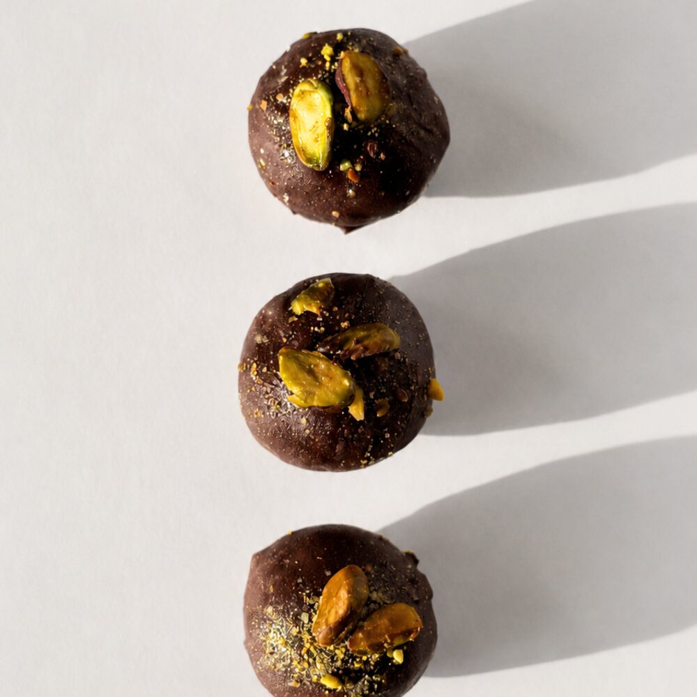 Three BITEY protein chocolates in dark Belgian chocolate topped with whole pistachios, in a row
