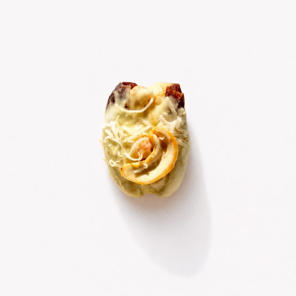 A royal date coated in white chocolate, topped with whole cashews and shredded coconut, photographed from above on white