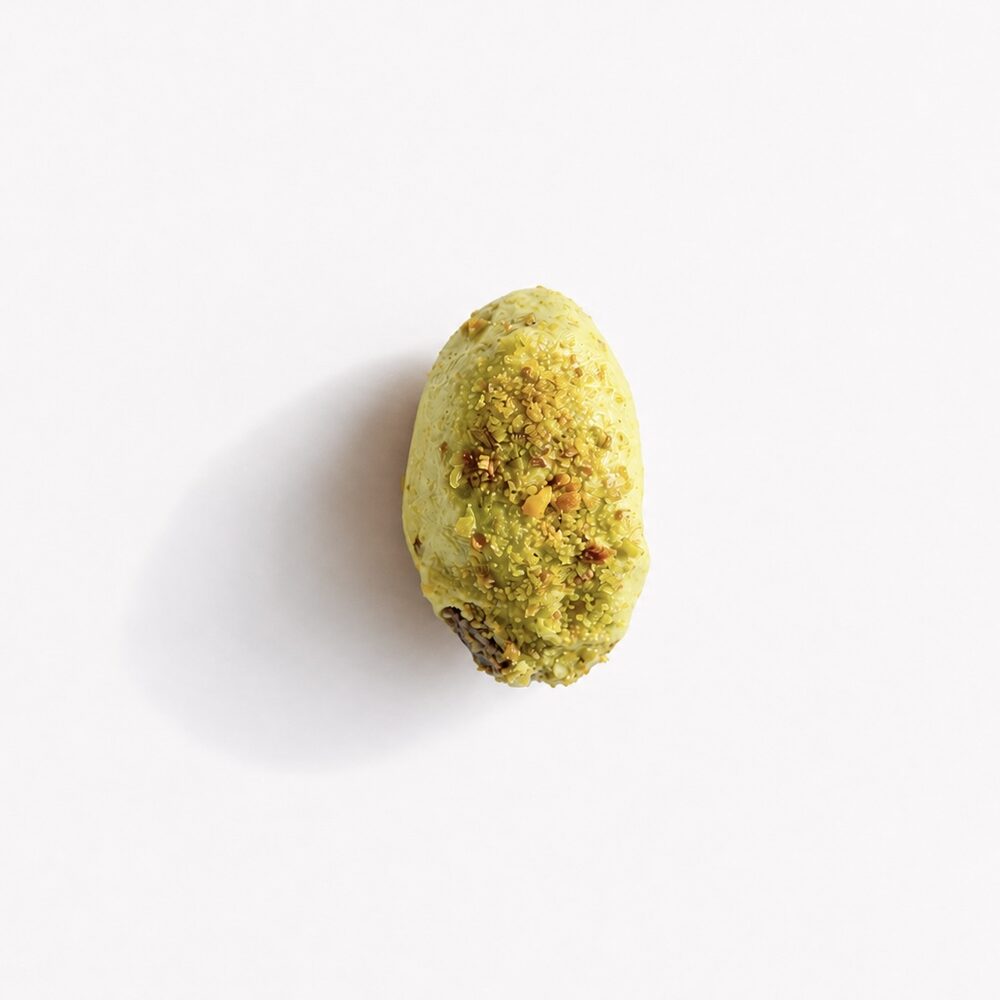 A royal date coated in green pistachio chocolate with crispy kataifi, photographed from above on white