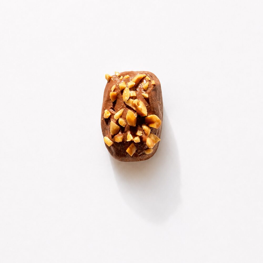 A royal date coated in milk chocolate and covered with chopped hazelnuts, photographed from above on white