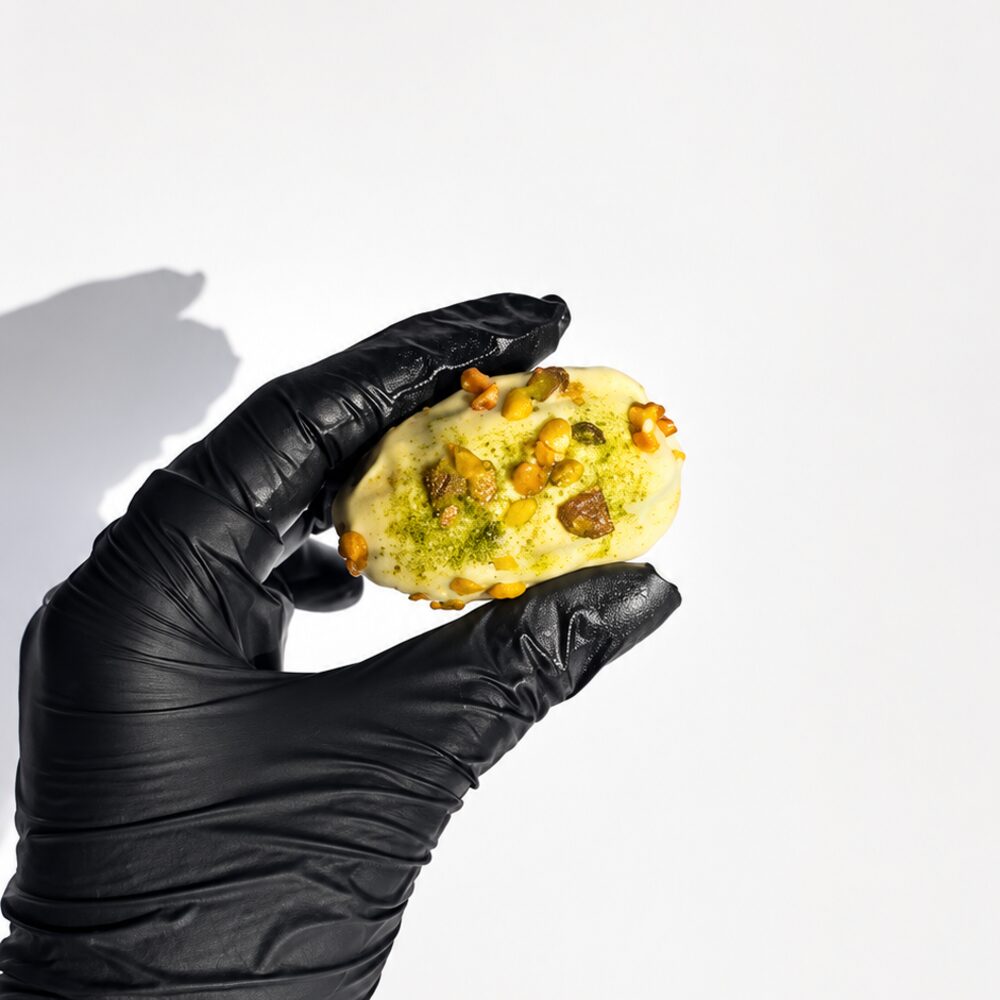 A royal date filled with pistachio cream and coated in white chocolate, cut open to show the green filling, on white