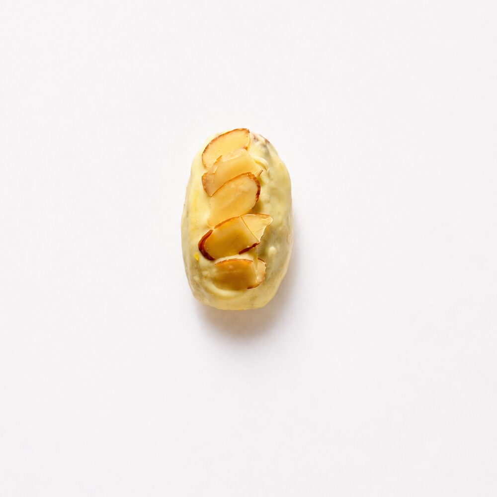 A royal date filled with coconut cream and coated in white chocolate, cut open to show the filling, on white