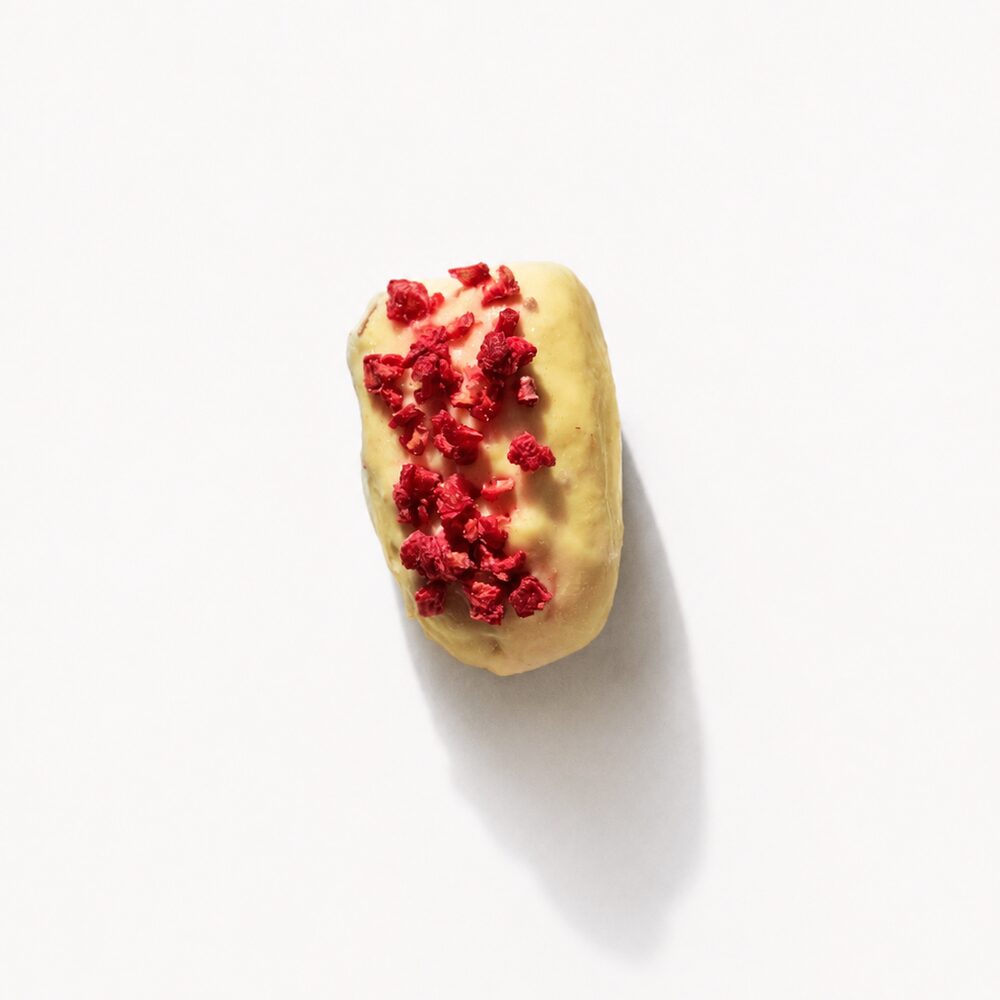 A royal date coated in white chocolate and scattered with freeze-dried berry pieces, photographed from above on white